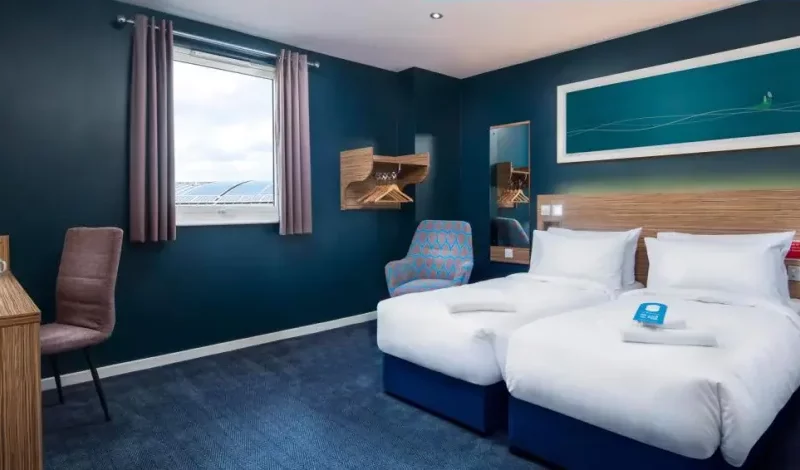 Modern teal hotel room with twin beds and ocean view.