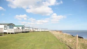 Coastal holiday homes overlooking the sea and grassy field.