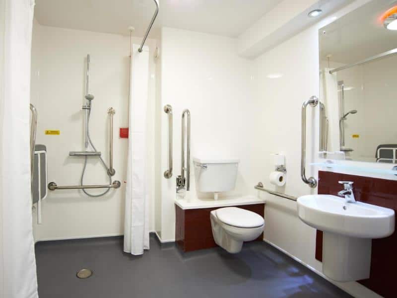 Accessible bathroom with safety handrails and white fixtures.