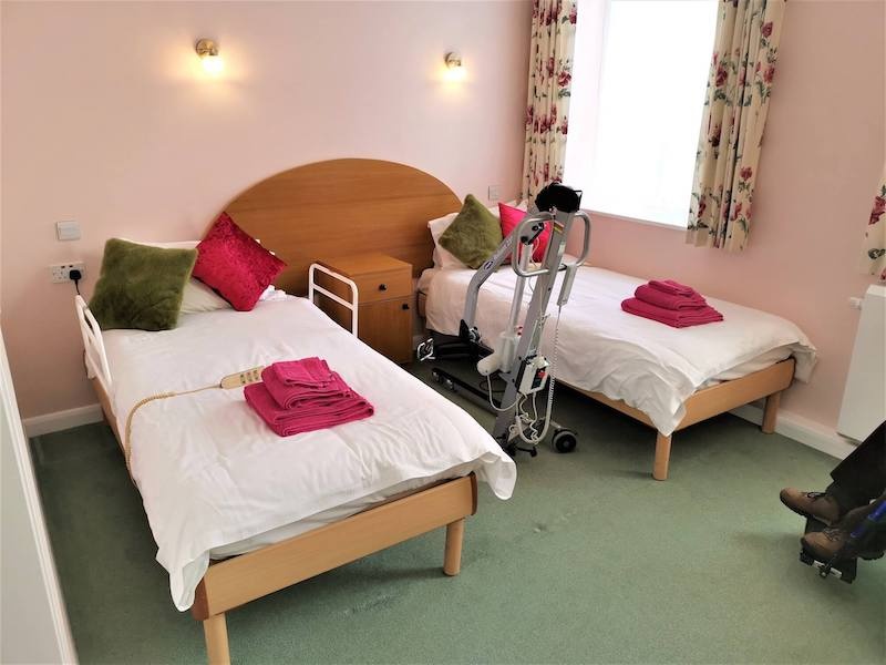 Accessible twin room with medical hoist and bright decor.