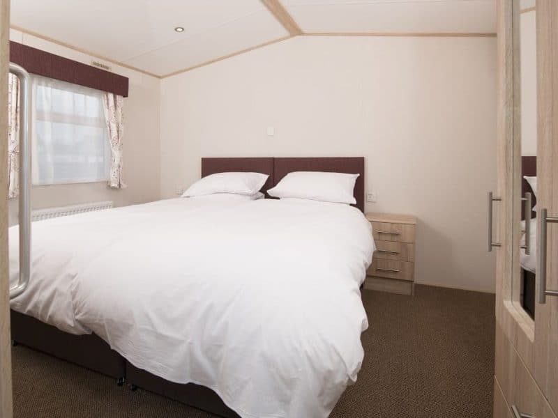 Minimalist bedroom with white bedding and wooden furniture.