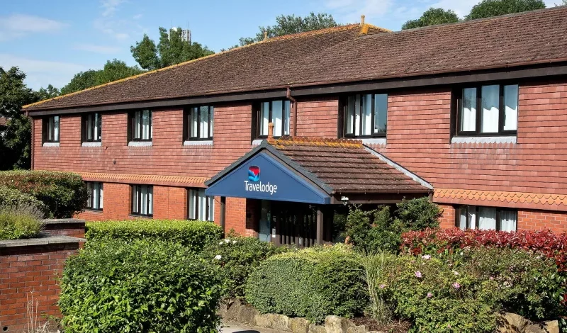 Travelodge hotel surrounded by lush gardens on sunny day.