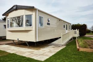 Modern beige mobile home with ramp in park setting.