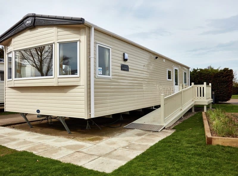 Modern beige mobile home with ramp in park setting.