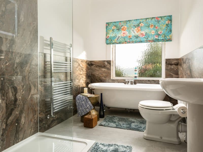 Modern bathroom with marble walls and floral window shade.