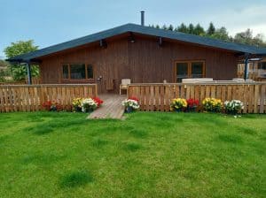 Wooden cabin with deck, hot tub, and colorful flowers.