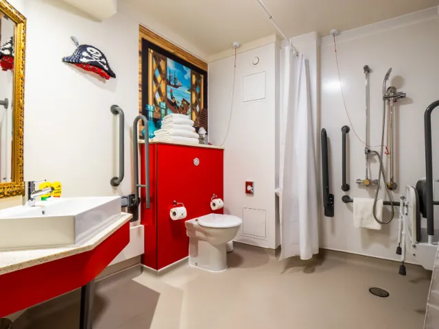 Accessible bathroom with red accents and assistive fixtures.