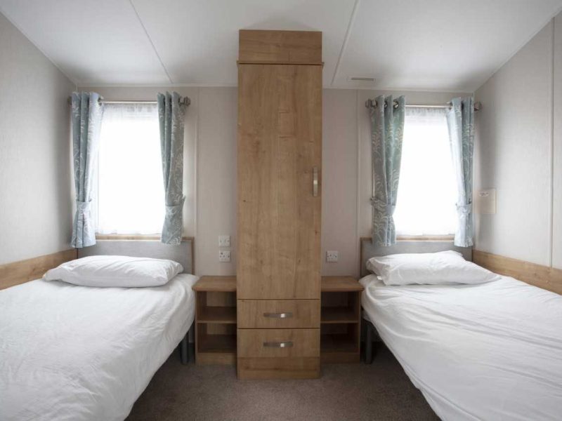 Simple twin bedroom with wooden furniture and natural light.