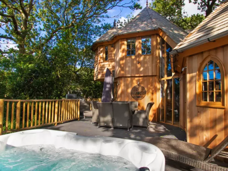 Luxurious wooden treehouse with hot tub in lush greenery.