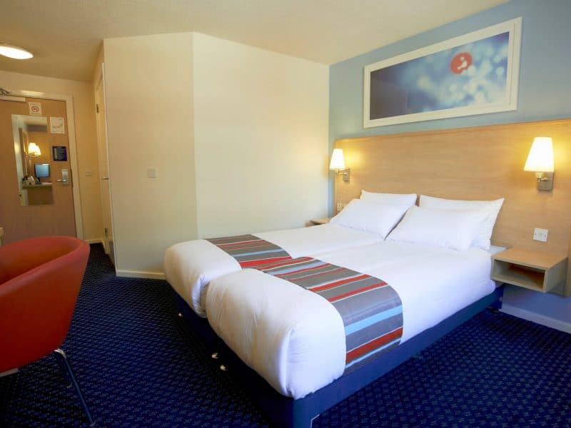 Bright, modern hotel room with large bed and red chair.