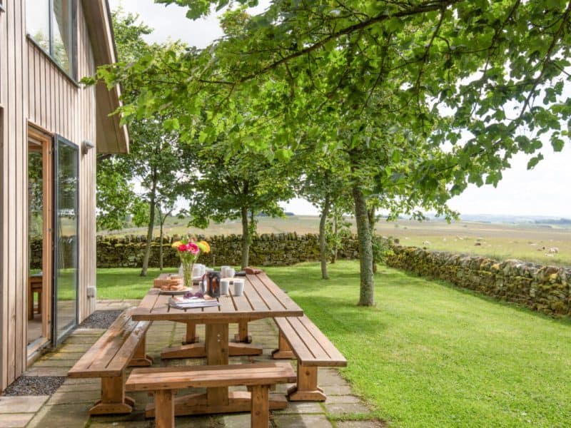 Rural house patio with wooden table and scenic view.