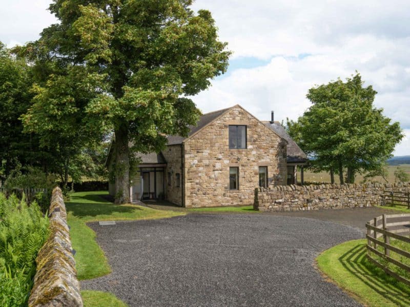 Stone house with driveway in rural landscape.