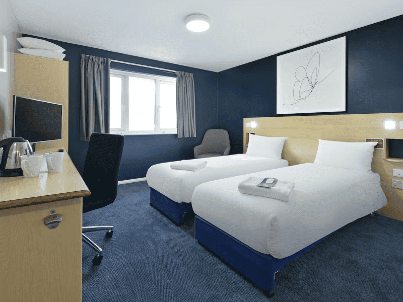 Modern twin bedroom with desk and TV in hotel.