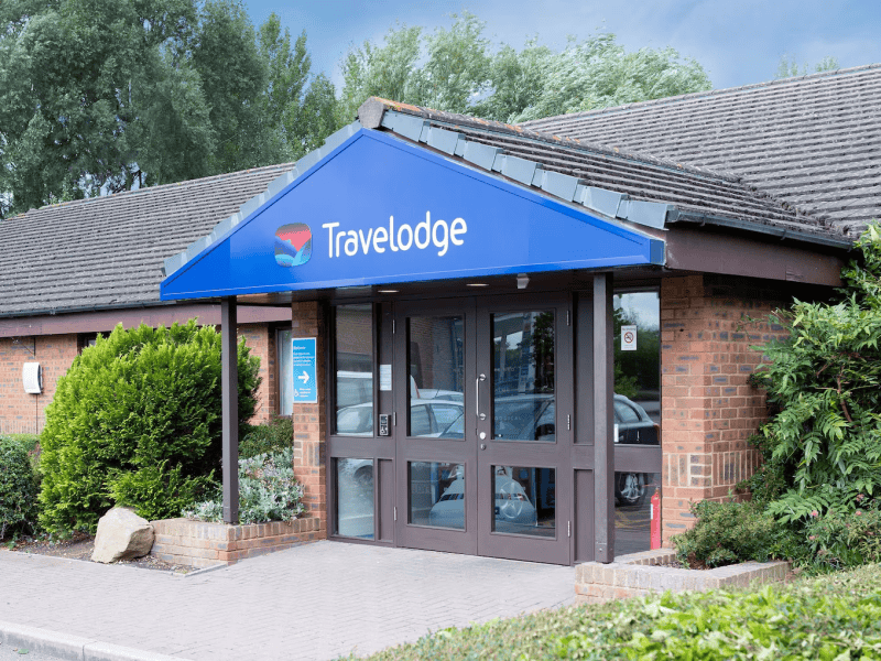 Travelodge hotel entrance with logo and landscaping.