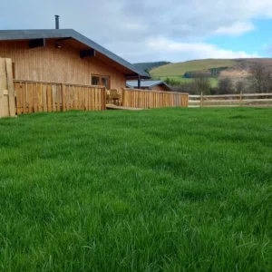 Wooden cabin with green lawn, rural landscape background.