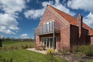 Brick house with balcony under sunny, cloudy sky.