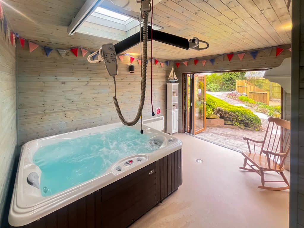 Indoor hot tub with ceiling hoist and open sliding door to garden.