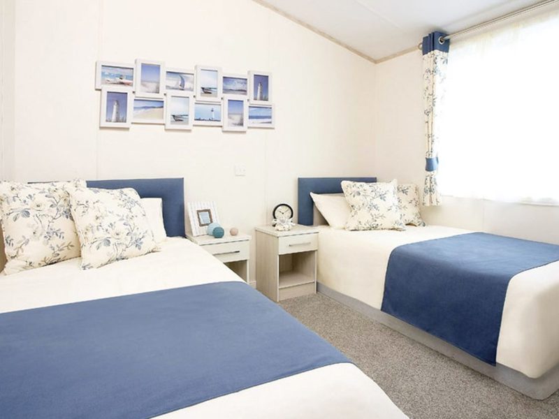 Bright twin bedroom with nautical decor and framed sea photos.