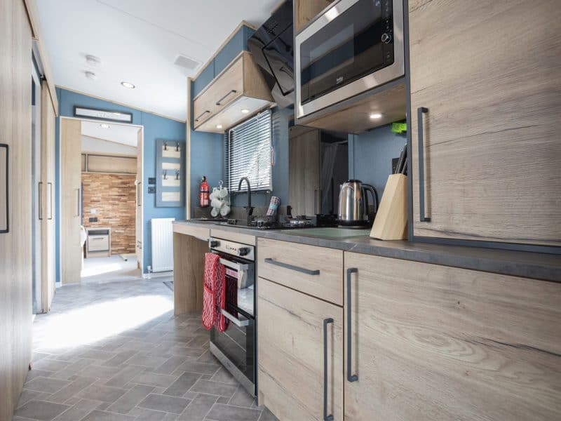 Modern RV kitchen with blue accents and wooden cabinets.