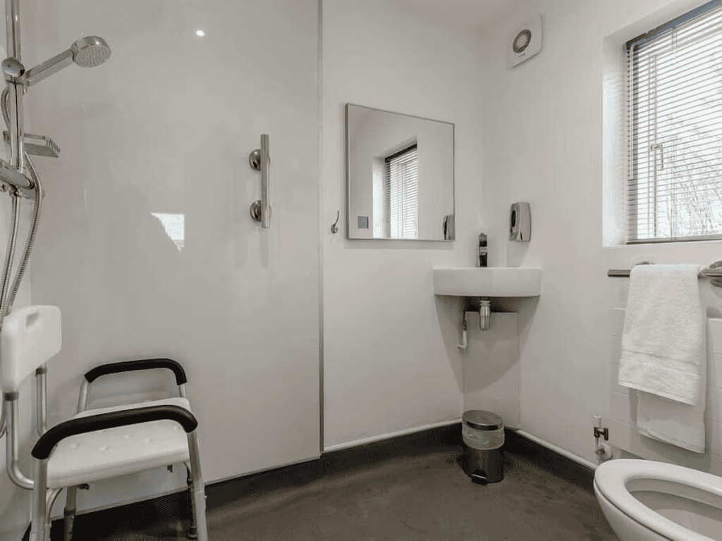 Accessible bathroom with a shower, sink, and support chair.