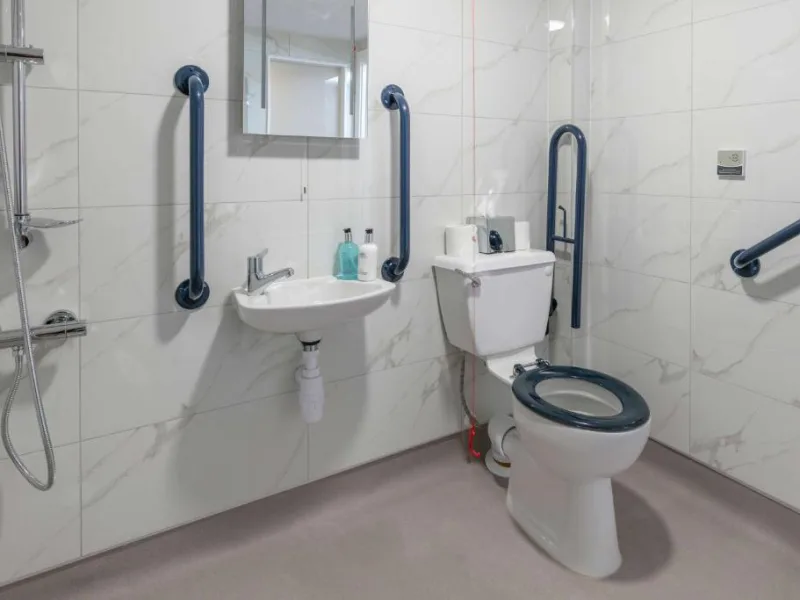 Accessible bathroom with safety grab bars and marble tiles.