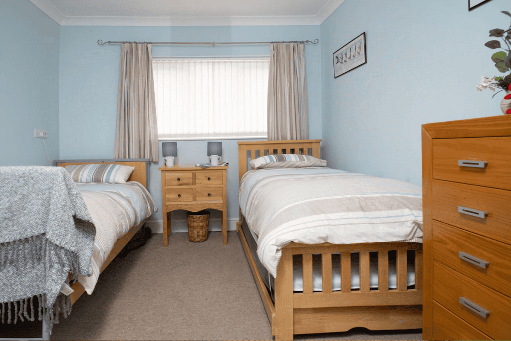 Twin beds in a tidy blue bedroom with natural light