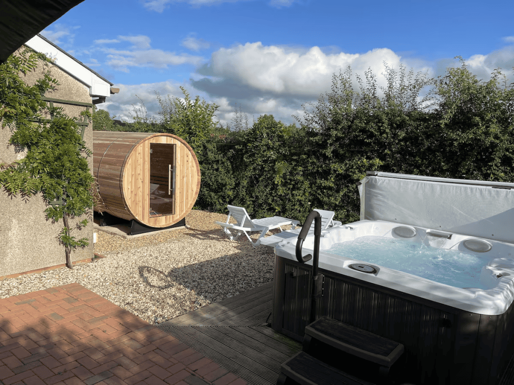 Backyard with hot tub, sauna pod, chairs under sunny sky