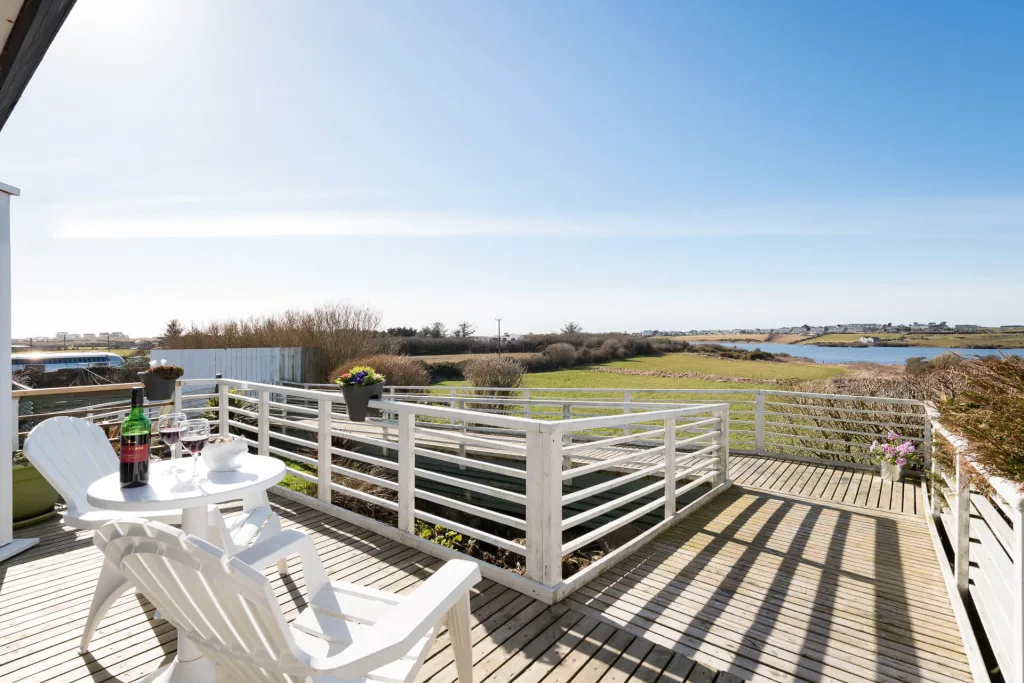 Sunlit deck overlooking scenic river with chairs and wine