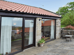 Stone cottage with glass doors, patio, and garden furniture.