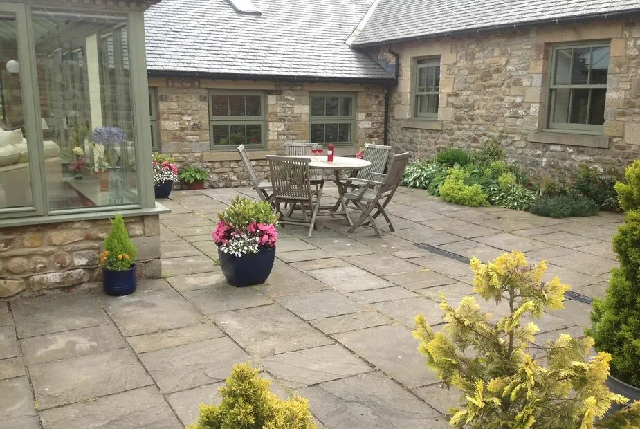 Stone patio with table, chairs, and colorful potted plants.