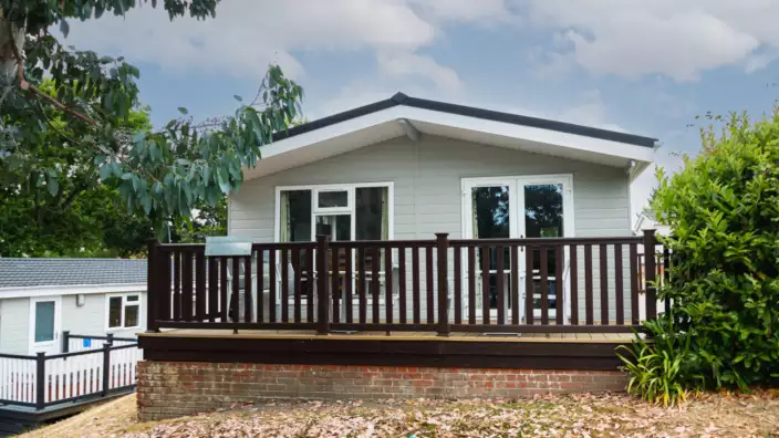 Small white house with wooden deck and greenery