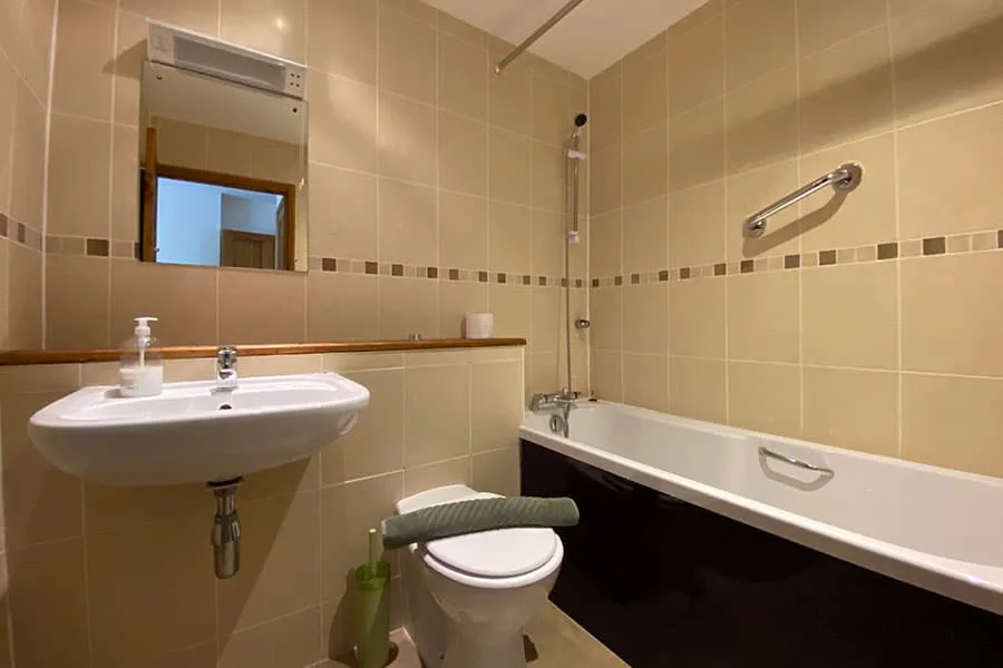 Beige tiled bathroom with mirror, sink, tub, and toilet