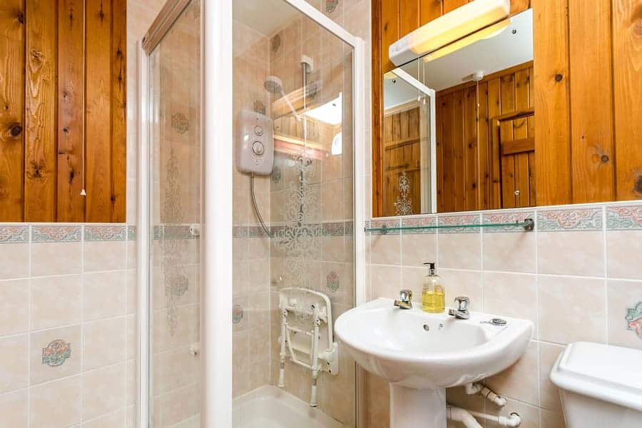 Small bathroom with shower, wooden panels, and sink