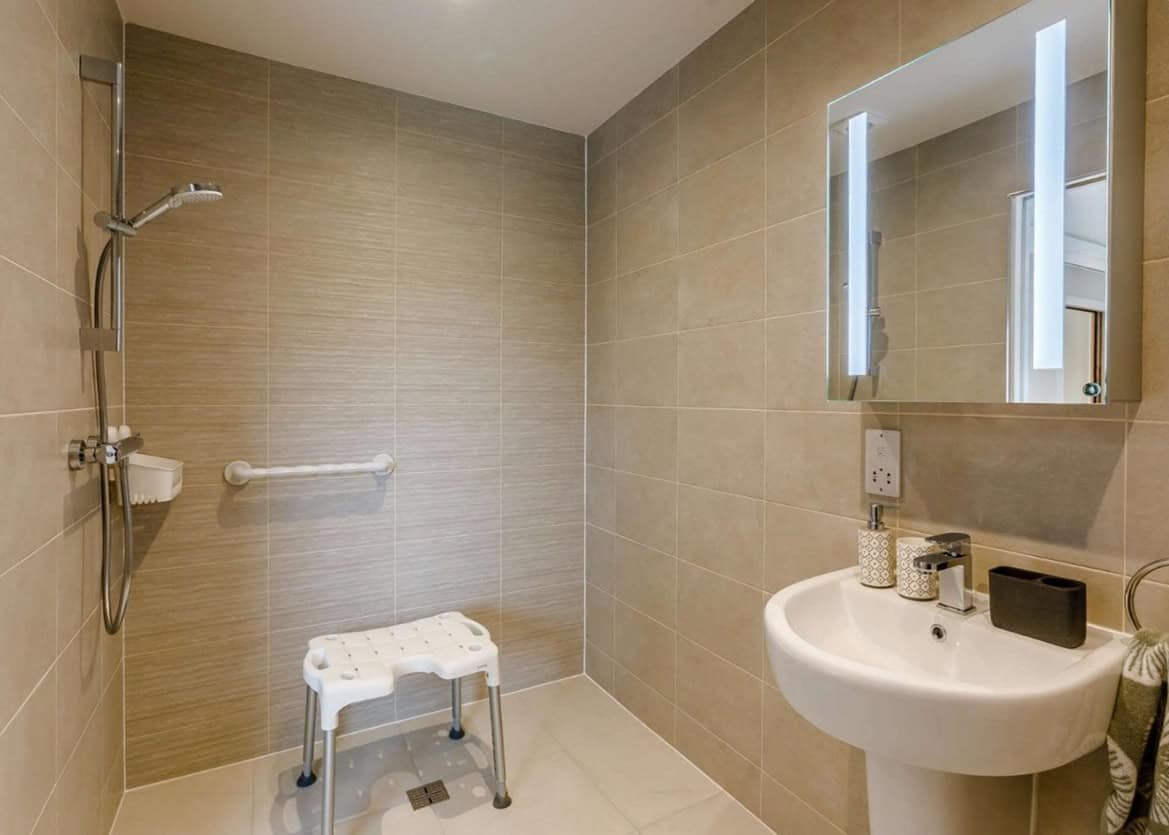 Modern bathroom with shower, sink, and accessibility seat.