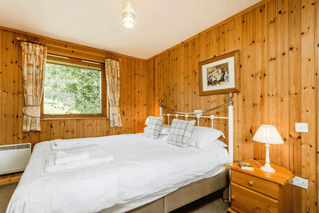 Cozy wooden bedroom with large window and white bedding