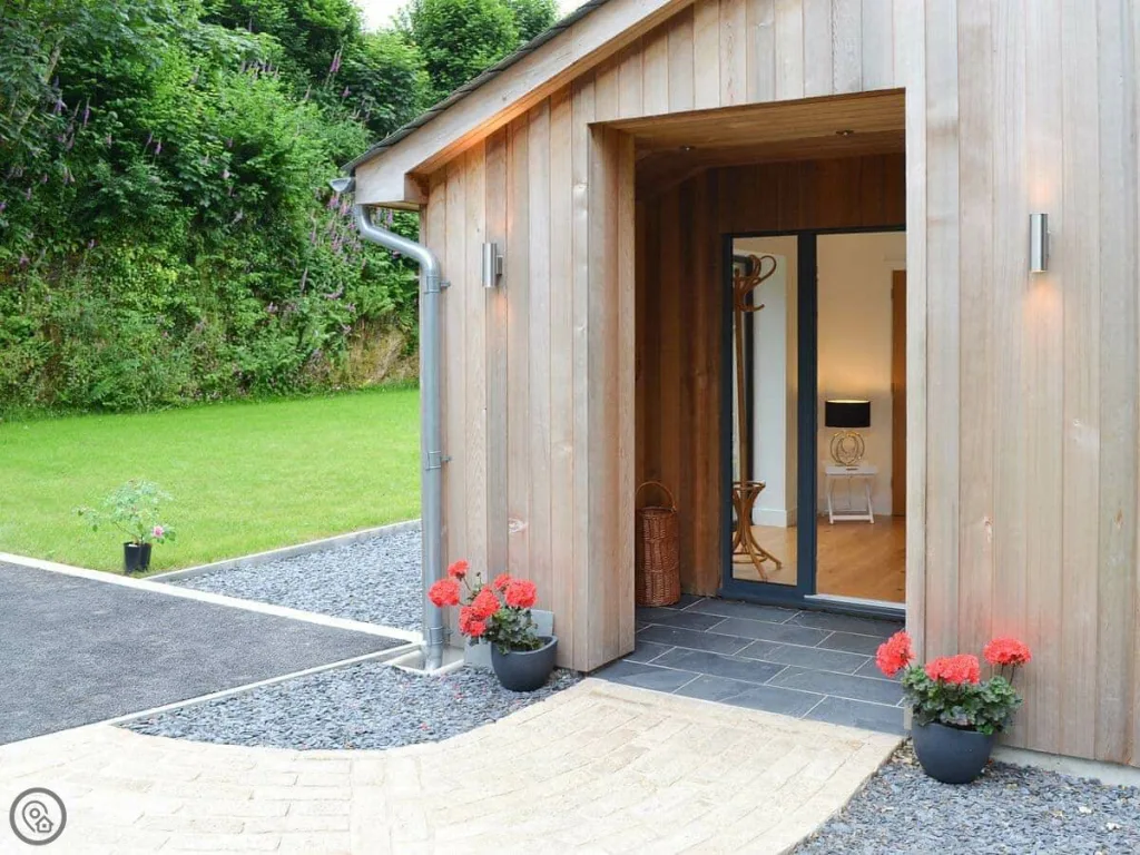 Modern wooden cabin entrance with red flowers and garden
