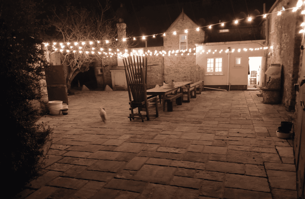 Stone courtyard with string lights and wooden furniture at night