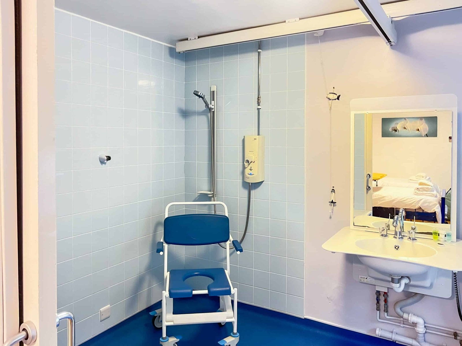 Accessible bathroom with shower chair, handrails, and blue tiles