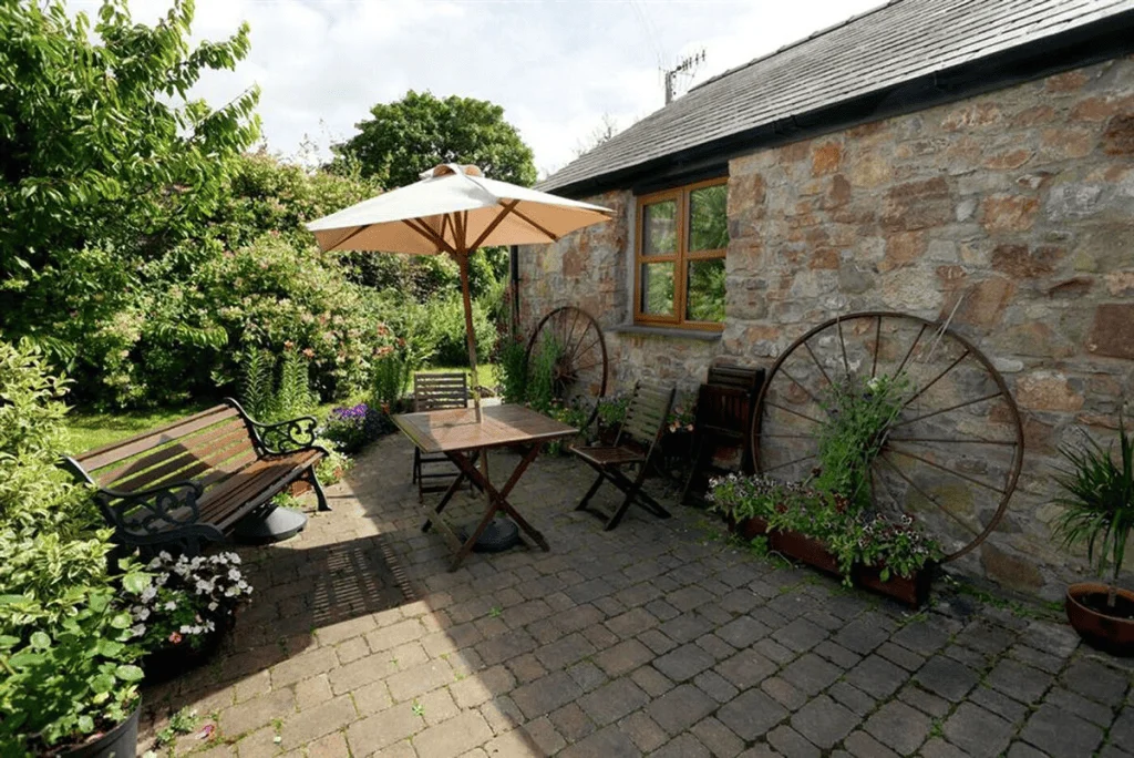 Quaint garden patio with umbrella, bench, and stone house.