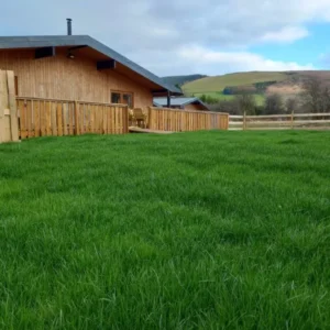 Wooden cabin with lush green lawn and hills backdrop