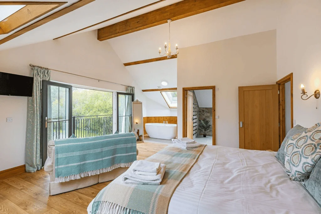 Spacious bedroom with balcony, bathtub, and exposed beams