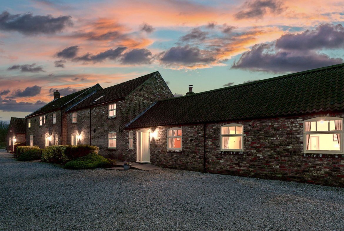 Charming farmhouse at sunset with illuminated windows.