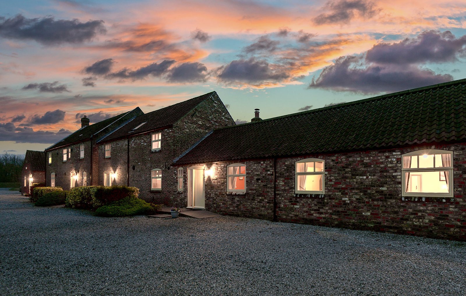 Charming farmhouse at sunset with illuminated windows.