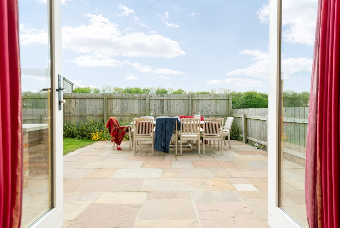Sunny patio with wooden chairs and red curtains.