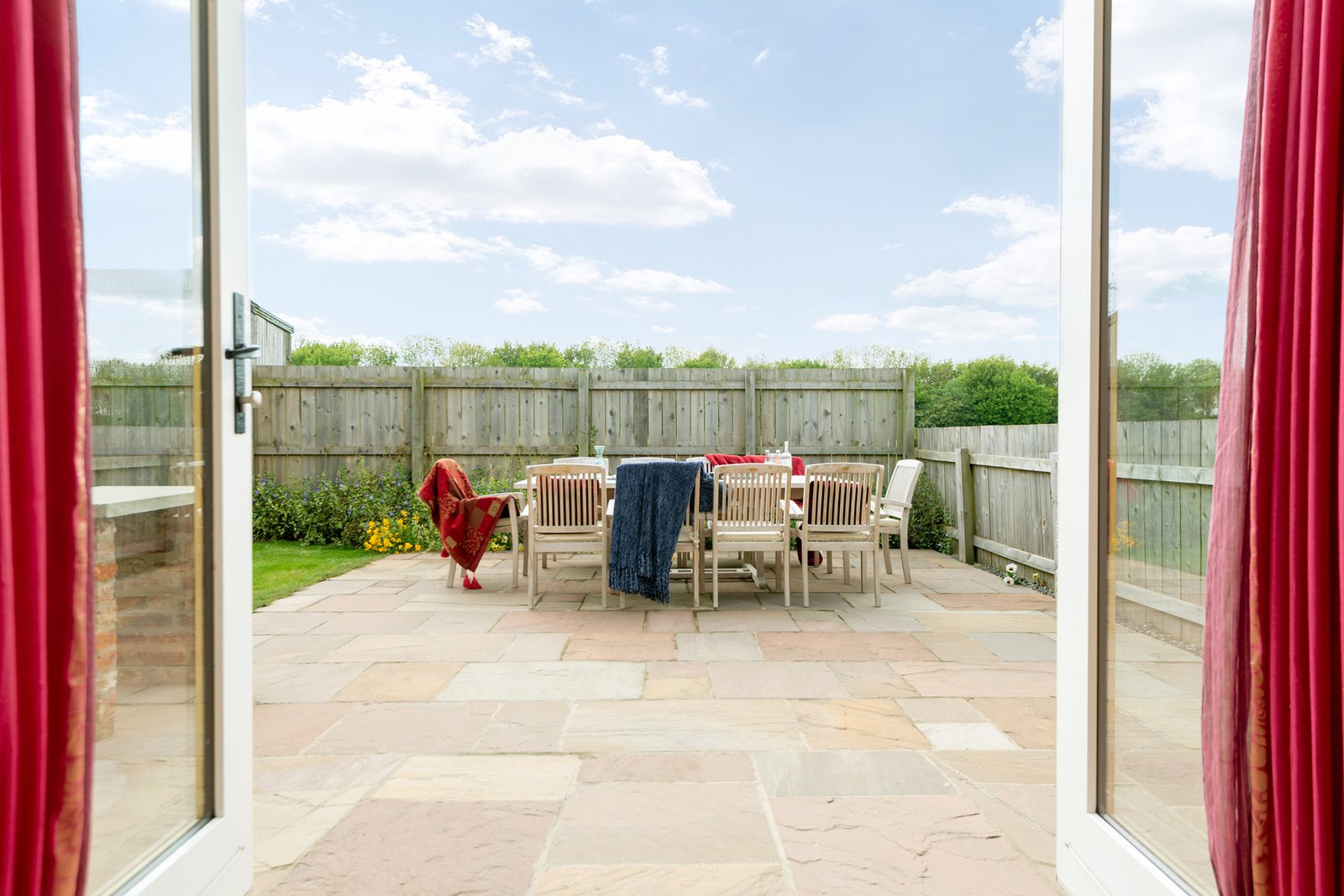 Sunny patio with wooden chairs and red curtains.