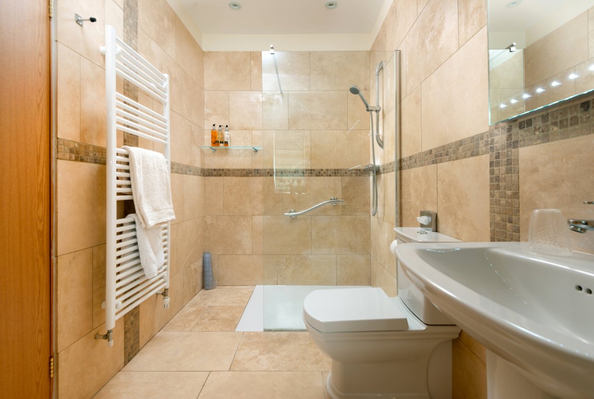 Modern beige tiled bathroom with shower and towel rail.