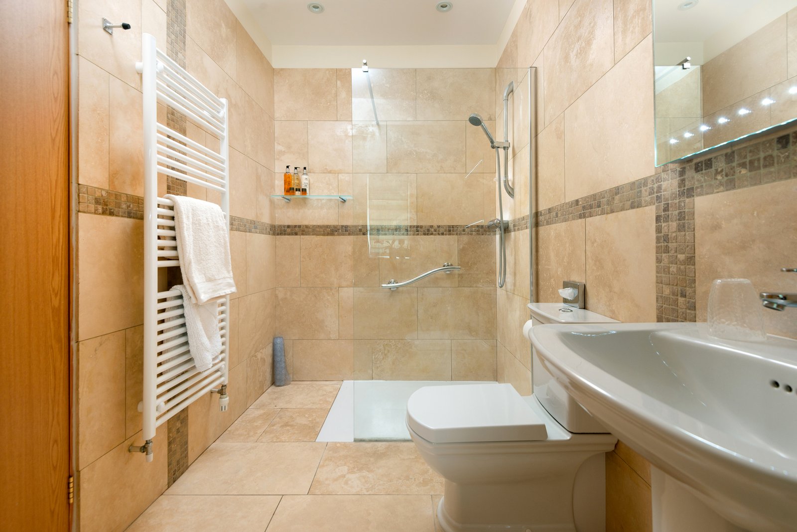 Modern beige tiled bathroom with shower and towel rail.