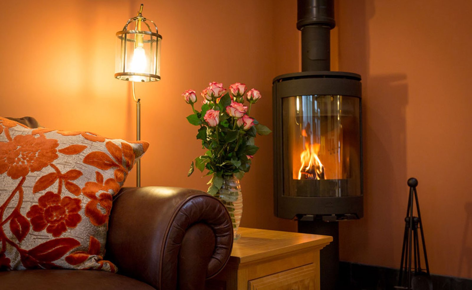 Cosy room with fireplace, flowers, and lamp.