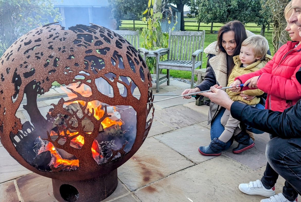 Family roasting marshmallows by decorative fire pit.