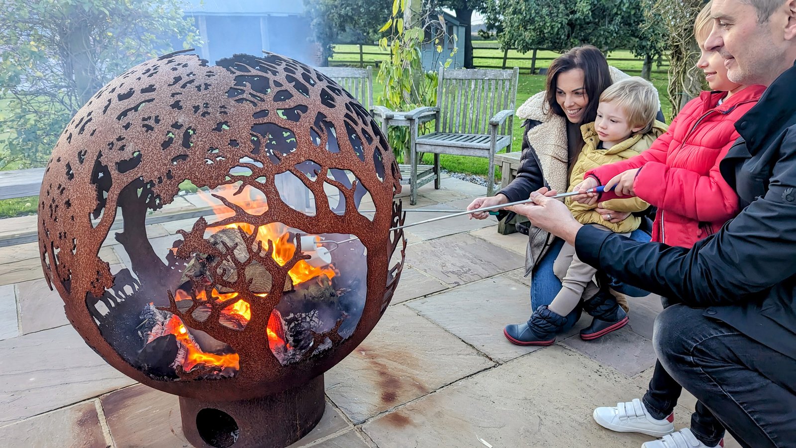 Family roasting marshmallows by decorative fire pit.